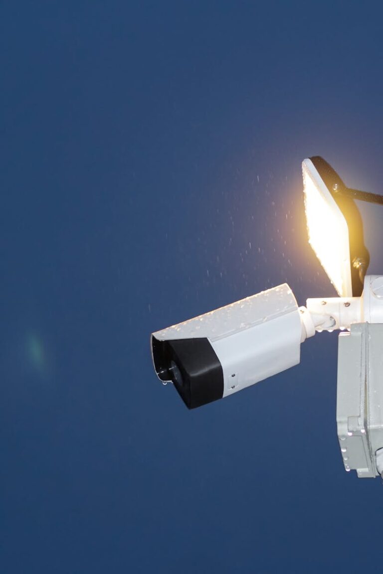 Low angle view of a security camera and light against a dark blue night sky.